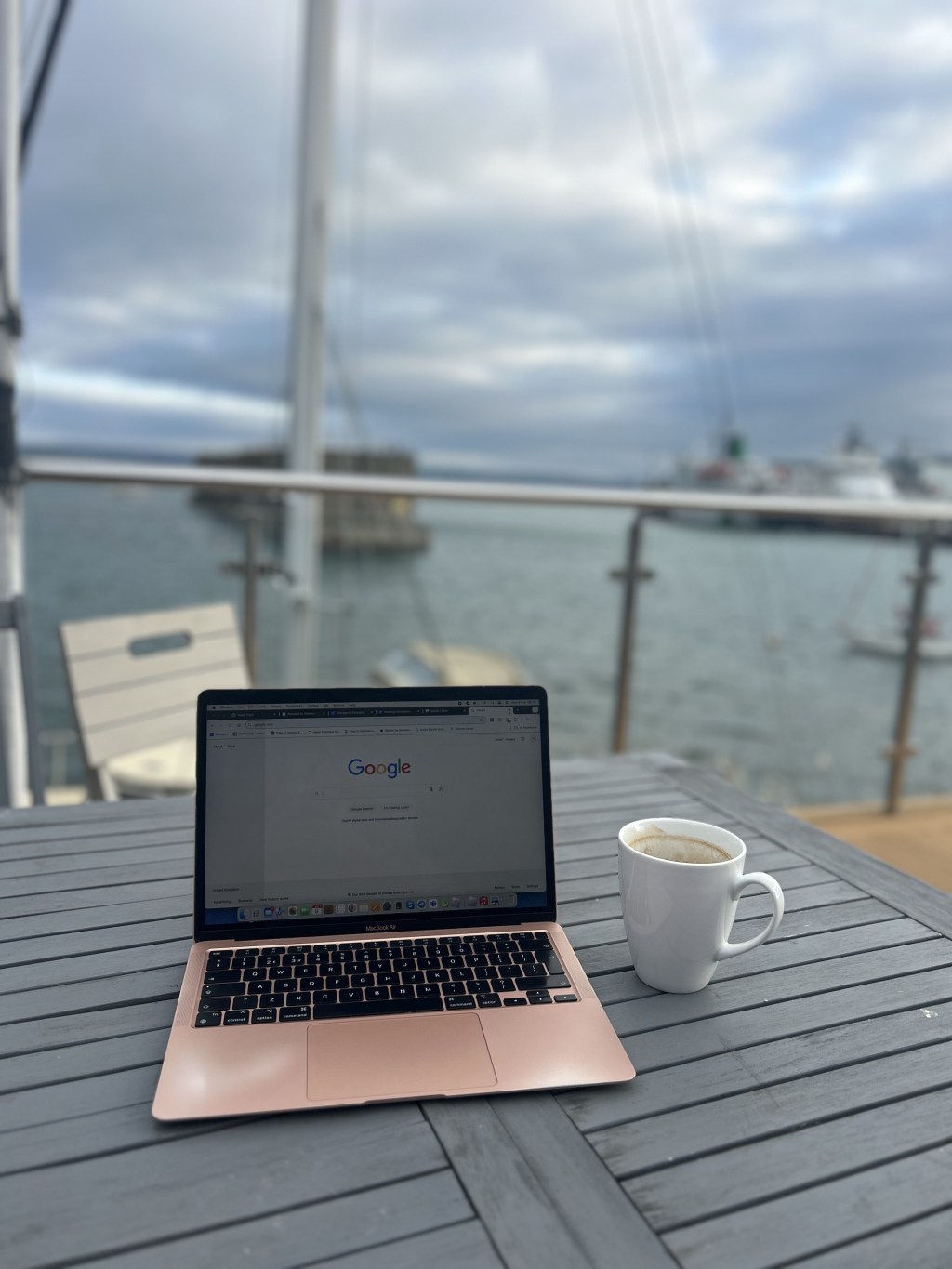 Sam's laptop and a coffee on a deck overlooking the water